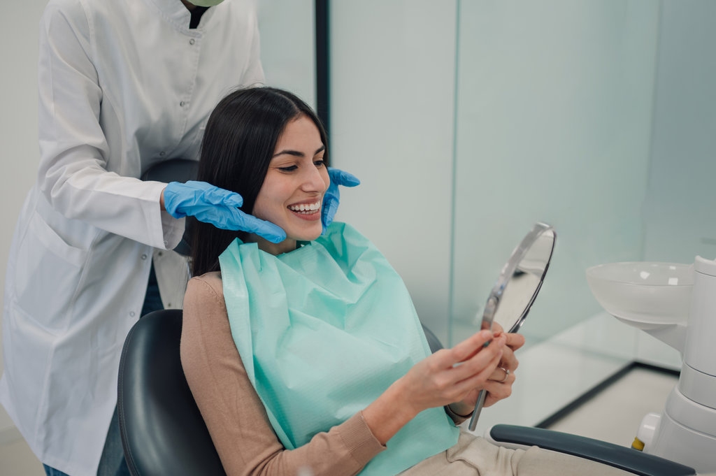 Dentist wearing gloves, smiling while showing a patient her perfect teeth in the mirror after a successful dental treatment at the clinic, radiating satisfaction and confidence
