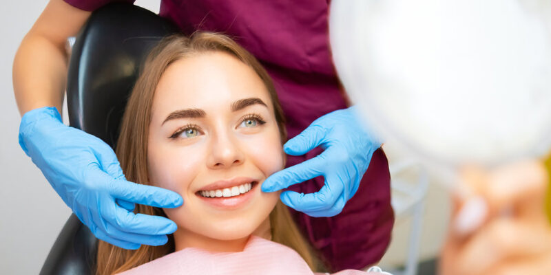 Dentist demonstrates the perfect smile of the patient after implatation of dental veneers or teeth whitening.