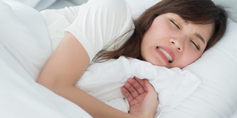 stressed woman with grinding teeth, bruxism symptoms; portrait of stressful, exhausted, tired sleeping woman grinding her teeth with stress; oral, dental care medical concept; asian adult woman model