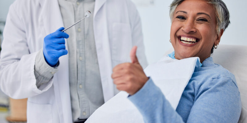 Happy woman, teeth and thumbs up for dentist in dental care, appointment or checkup at clinic. Senior female person smile with like emoji or yes sign in tooth whitening, cleaning mouth or gum care