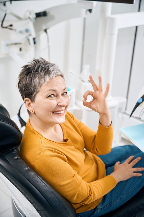 Smiling woman dental practitioner client showing ok gesture sitting on examination chair after the appointment, satisfied with caring approach and good oral hygiene