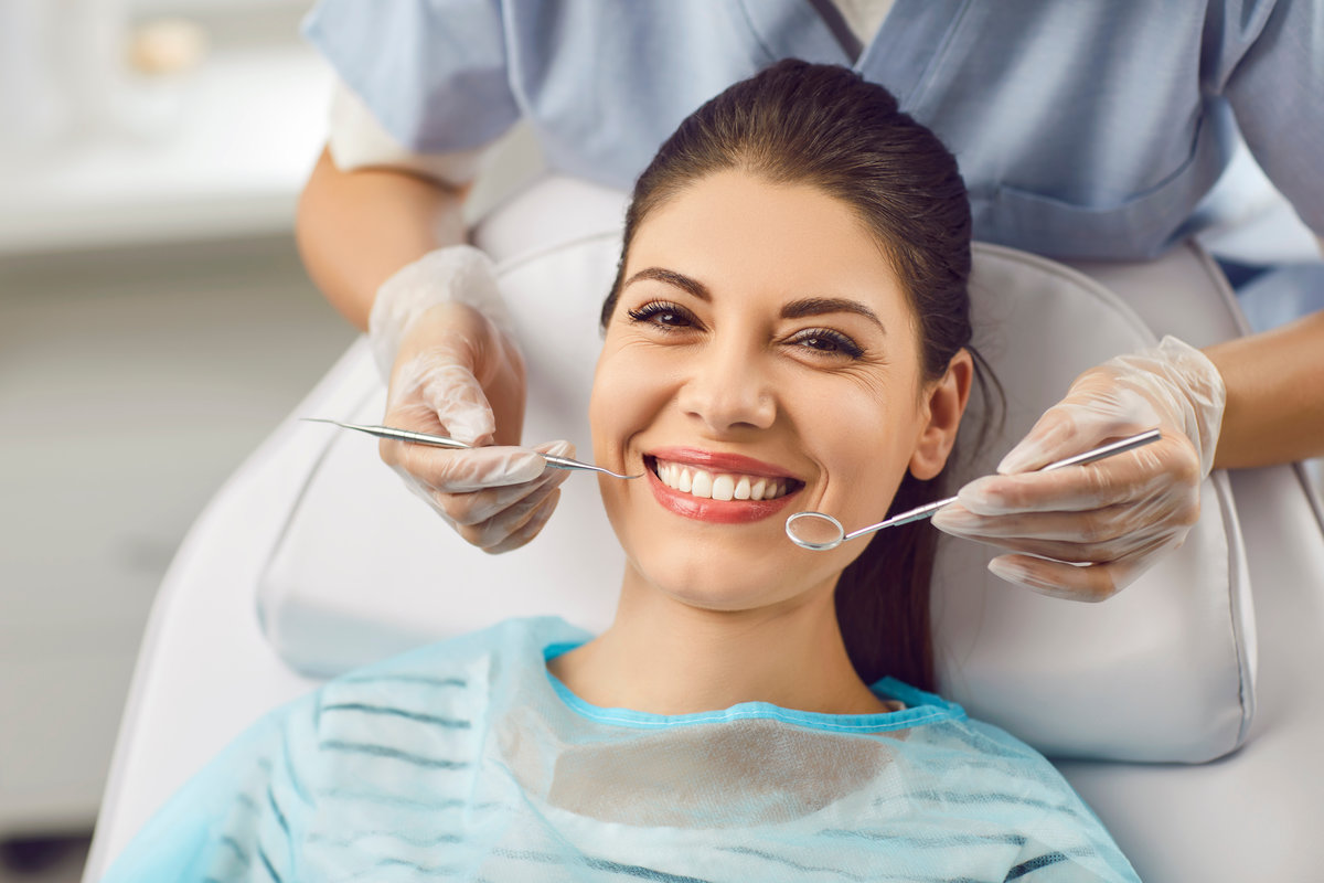 Portrait of a smiling patient with dentist doctor is checking teeth with a dental instrument. Dental care provided during the medical visit, regular dentistry check up for maintaining oral health.