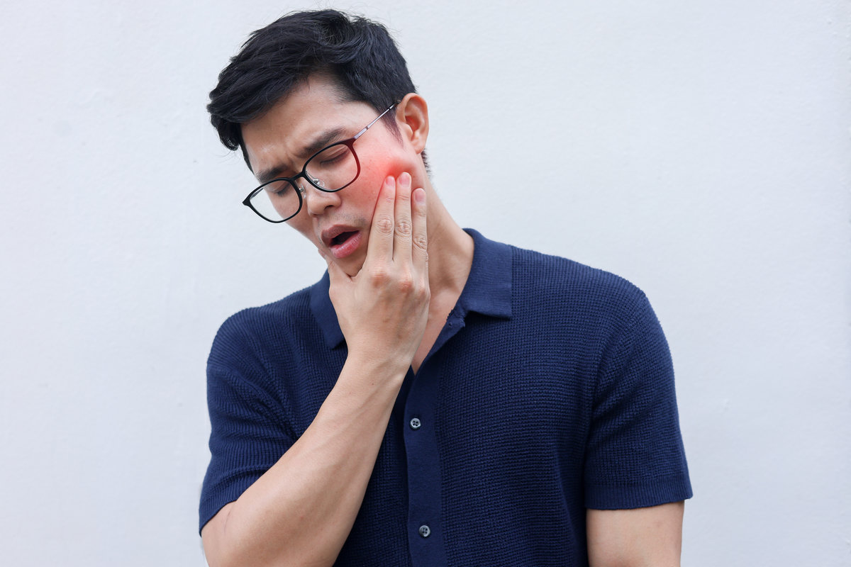 close up young asian man frown and use hand to massage on cheek after feeling pain or hurt from tmj muscle symptom at home for un healthy lifestyle and treatment concept