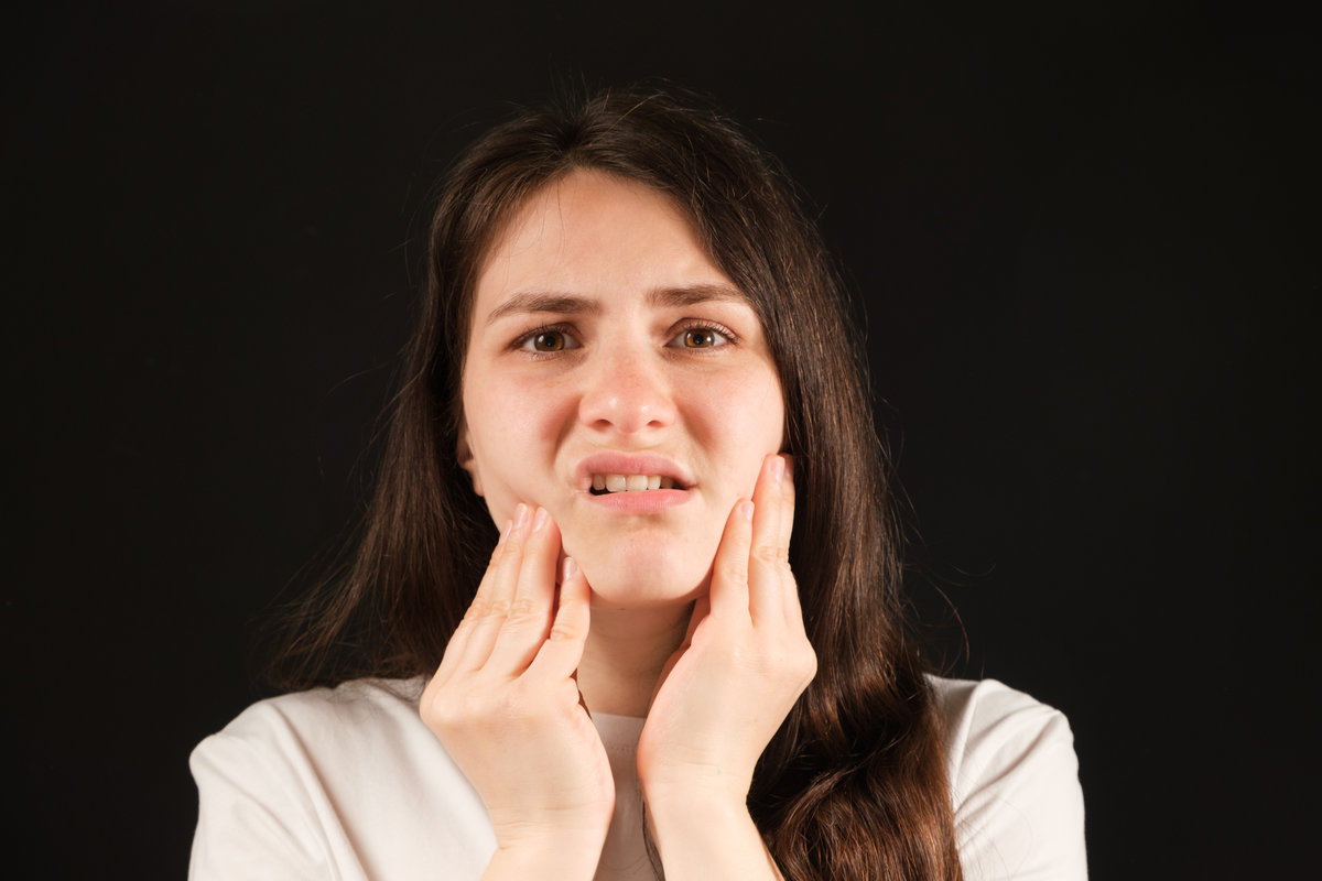 A woman holds her hands to a sore temporomandibular joint, dysfunction and pain, dislocated jaw, problems of wisdom teeth