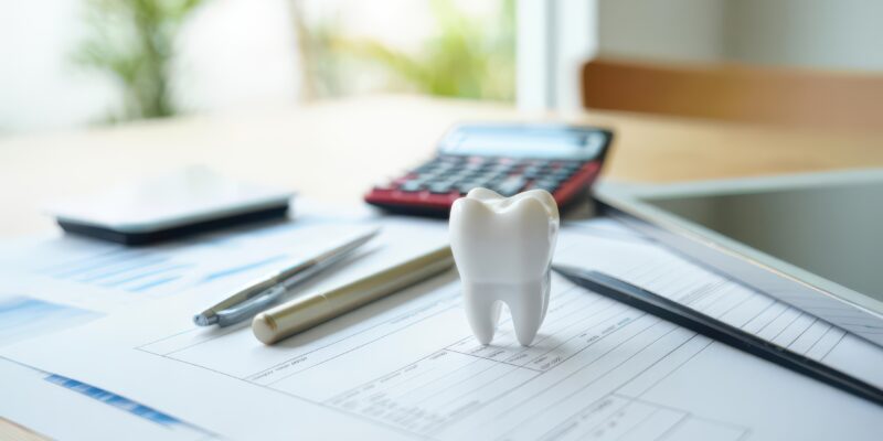 Tooth model on financial documents in dental office environment symbolizing dental business planning, insurance, or cost analysis in the healthcare sector.