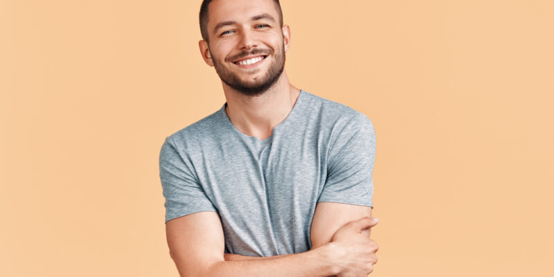 Happy smiling handsome man with crossed arms looking to camera over beige background. Emotions concept