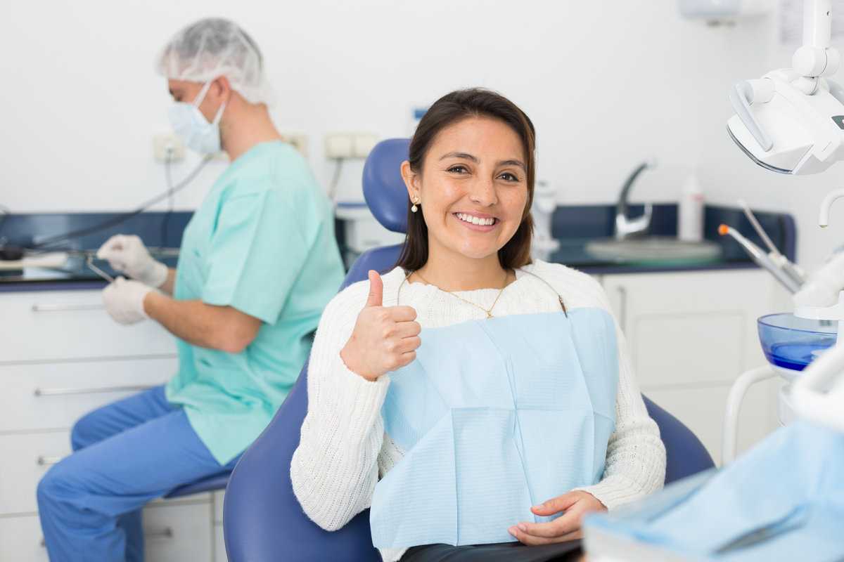 Portrait of smiling satisfied american woman visiting dentist giving thumbs up