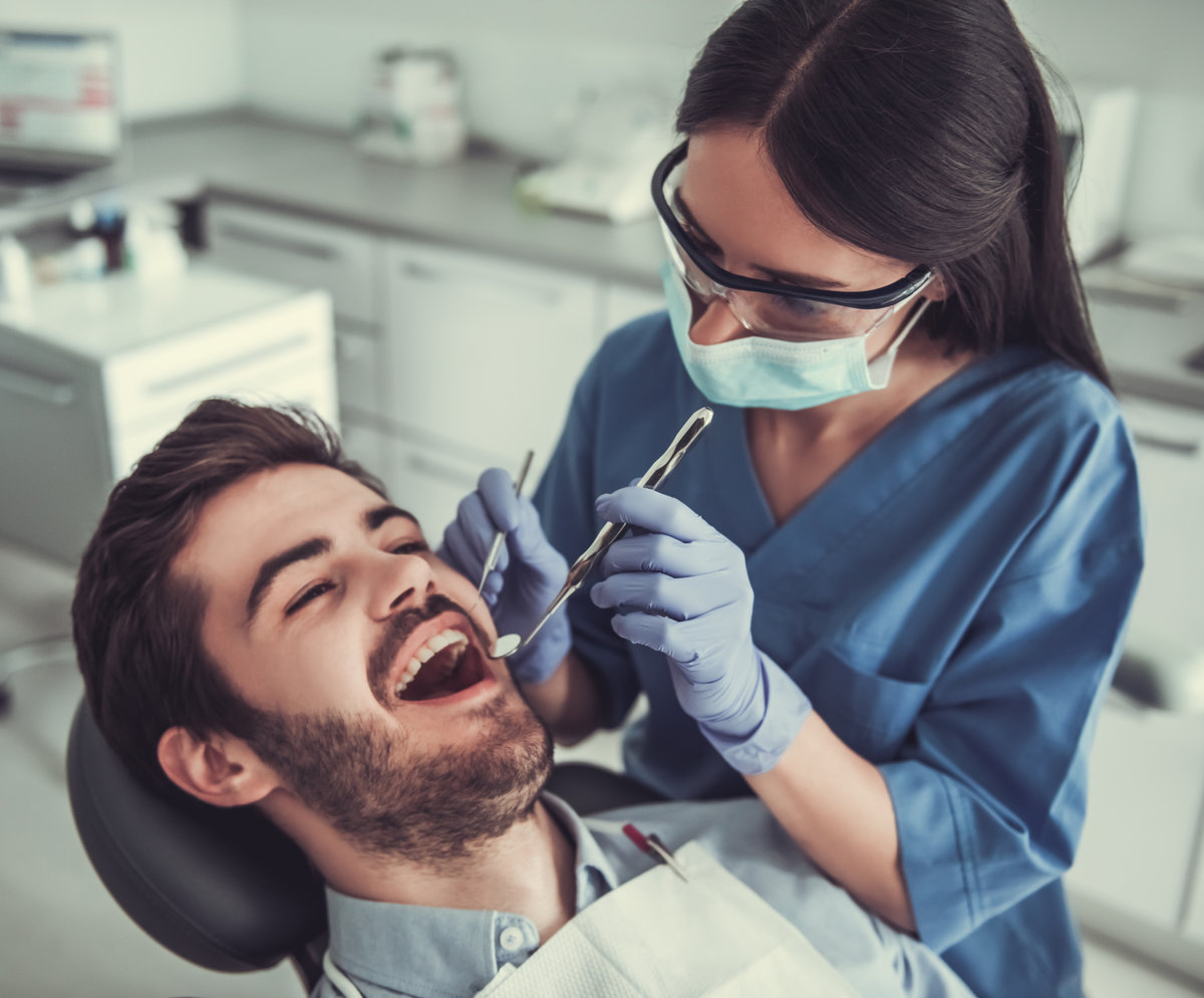 Handsome young patient is sitting in chair and smiling while visiting a beautiful female dentist