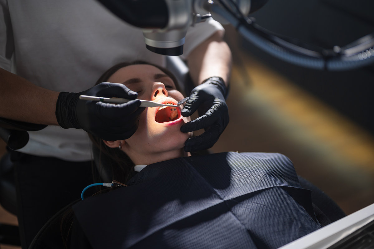 Restorative Dentist Operating On Patient Mouth Using Microscope And Rotary Instruments, Gloved Hands