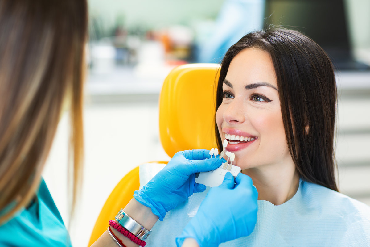 Young beautiful women in dentist chair, check and select the color of the teeth.