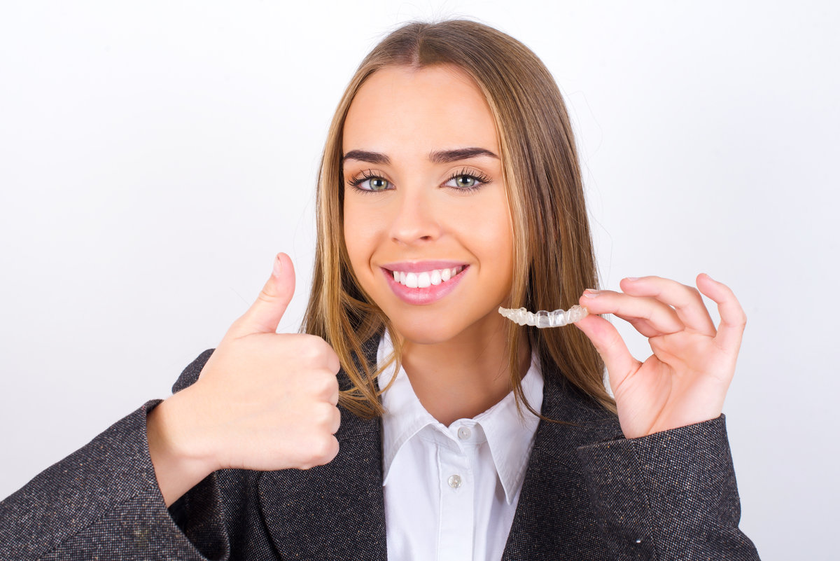 MODEL holding an invisible braces aligner and rising thumb up, recommending this new treatment. Dental healthcare concept.