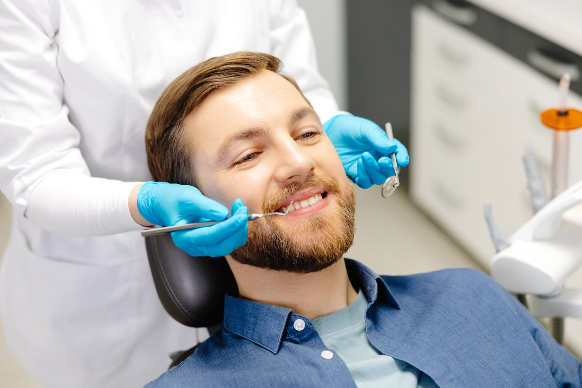 Portrait of happy man sitting at dentist chair in modern clinic and smiling. Patient enjoying dental treatment with professional stomatolog.