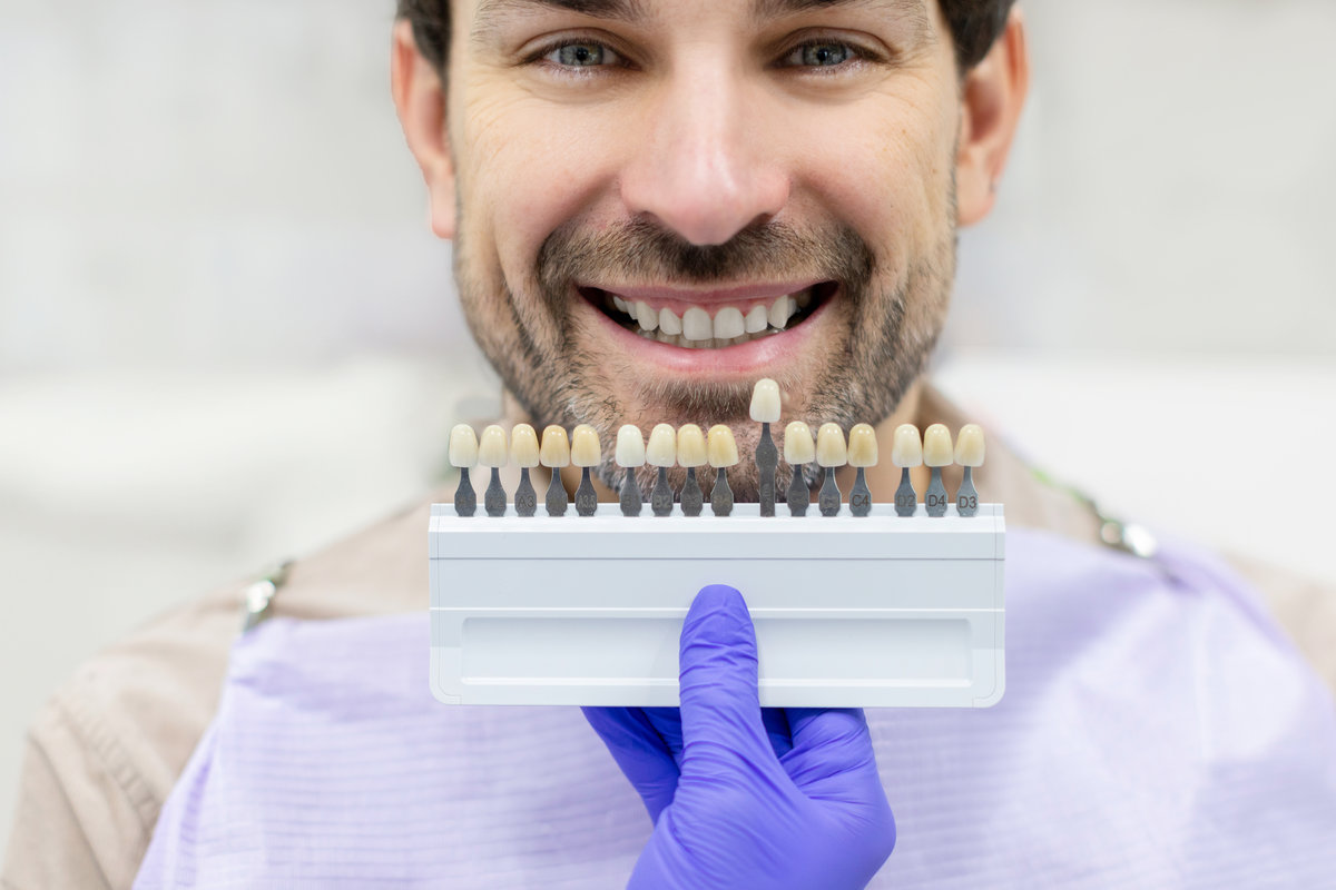 Dentist holding dental teeth shade guide chart, choosing right emanel color for male patient, closeup shot