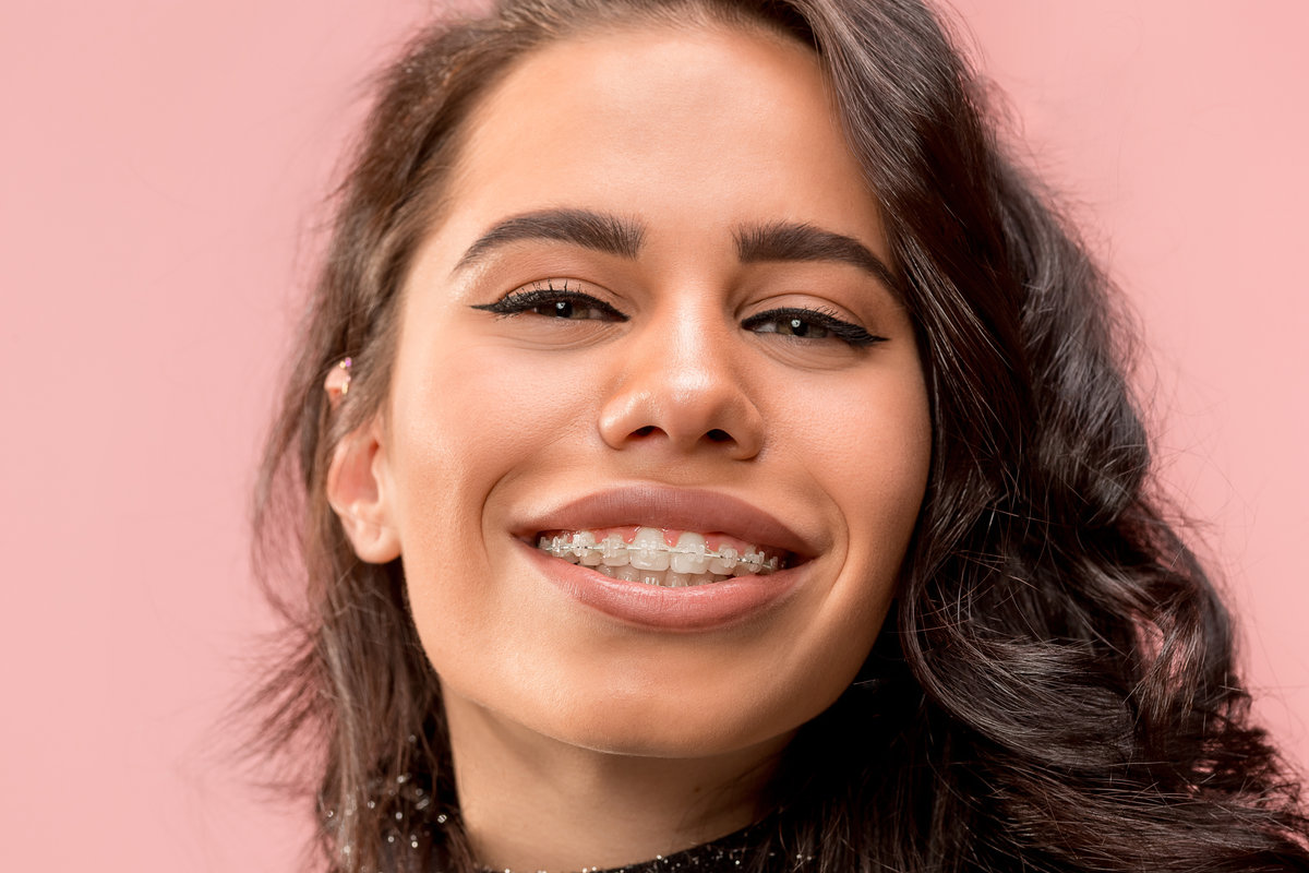 Beautiful young woman with teeth braces on pink