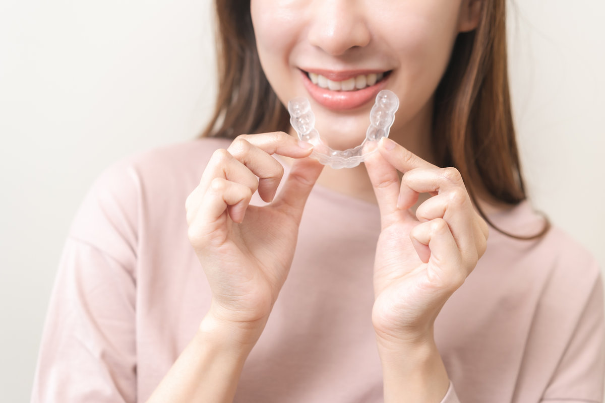Dental invisible braces, beautiful smiling asian young woman holding invisalign braces, wearing orthodontic silicone trainer, white smile using invisible whitening tray. Stomatology, dental healthcare