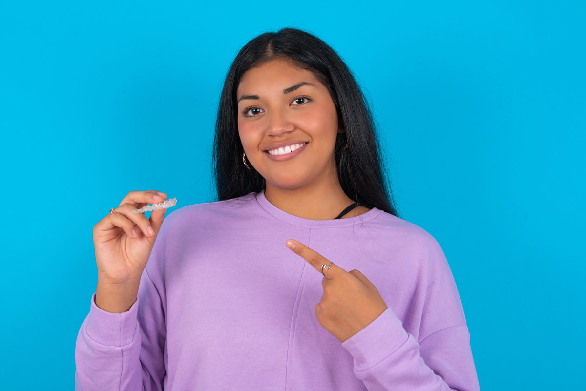 MODEL holding an invisible aligner and pointing at it. Dental healthcare and confidence concept.