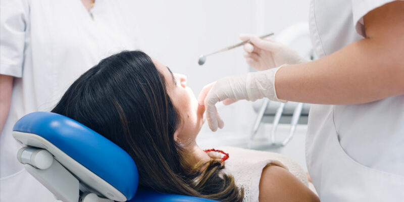 Dentist in protective gloves checking a patient's mouth with dental tools during a routine oral hygiene examination at a clinic