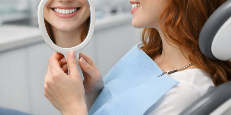Young Redhead Woman Admiring Her Smile in Handheld Mirror, Dental Patient